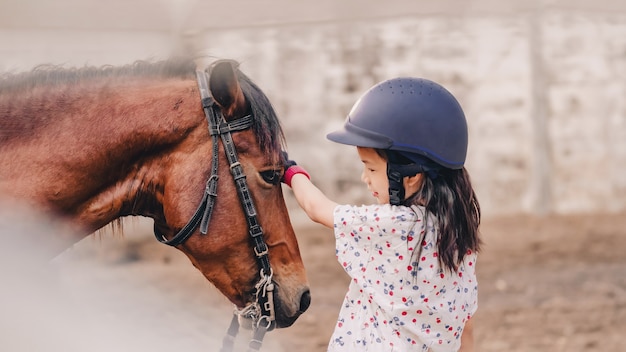 Asian school kid girl with horse riding or practicing horse riding at a horse ranch