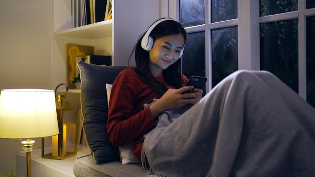 Asian woman listen to music in living room at night. Lifestyle and relaxing at home.