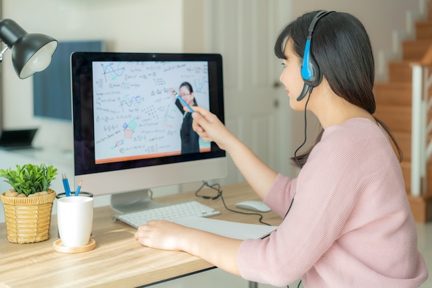 Photo asian woman student video conference e-learning with teacher on computer in living room at home.