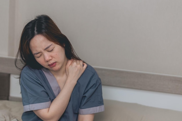 Foto donna asiatica che soffre di dolore alla spalla e alla tensione del collo a casa