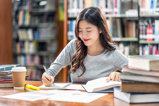 Photo asian young student in casual suit reading and doing homework in library of university or colleage