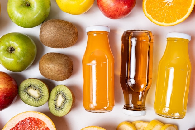 Foto assortimento di succhi di frutta in bottiglie di vetro tra i frutti su sfondo bianco vista dall'alto