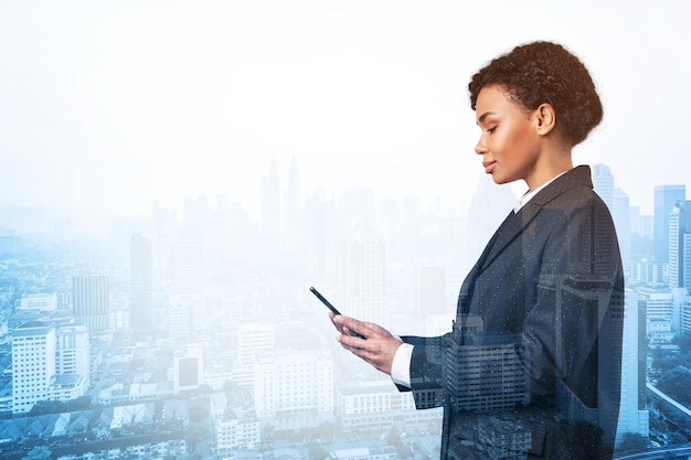 Attractive black African American business woman in suit using smart phone and thinking how to tackle the problem new career opportunities MBA Kuala Lumpur on background Double exposure