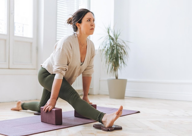 Attractive middle aged brunette woman in sportswear ptactice yoga with equipment in the light studio