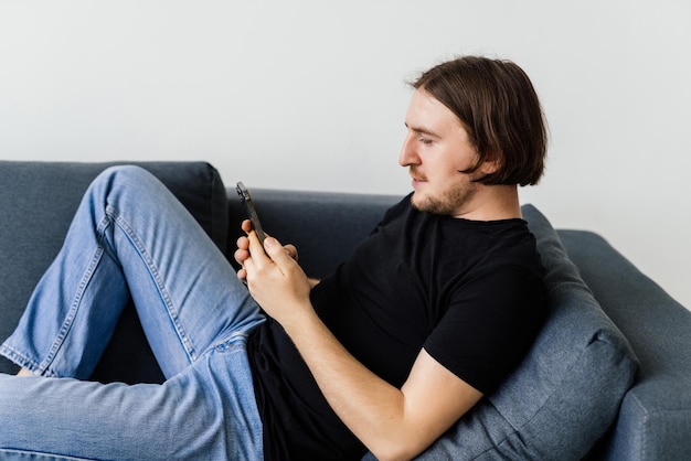 Attractive young man sitting on a floor in the living room using mobile phone