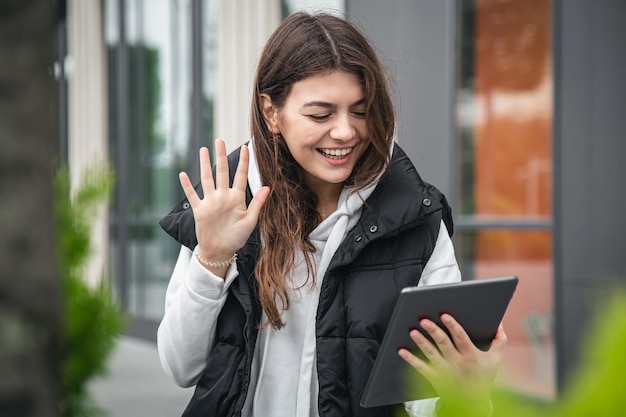 Attractive young woman uses a tablet communicates by video call outside