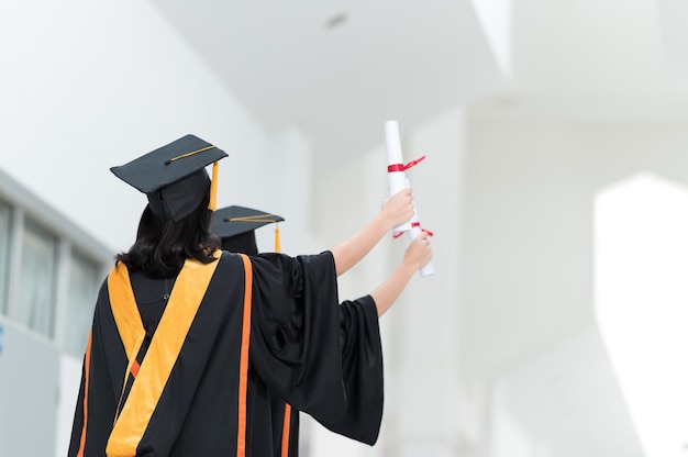 The back image of a female college student graduates wearing a black hat yellow tassel