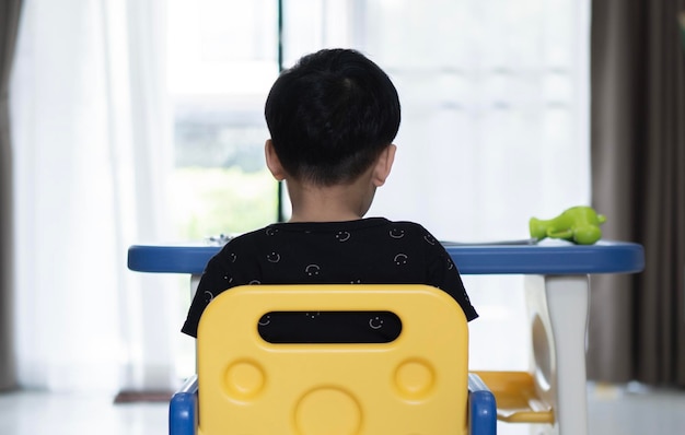 Back view of Asian child siting at table and doing school homework