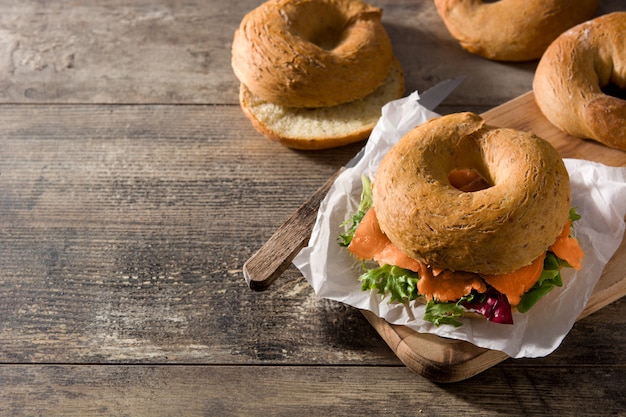 Photo bagel sandwich with cream cheese, smoked salmon and vegetables on wooden table, copy space