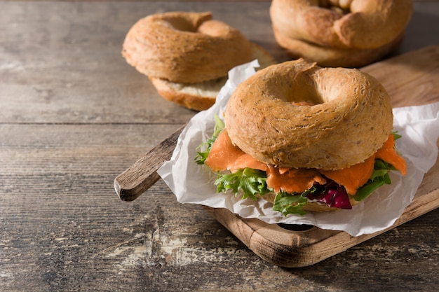 Photo bagel sandwich with cream cheese, smoked salmon and vegetables on wooden table