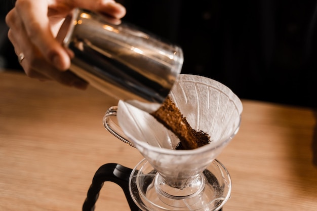 Photo barista pour ground coffee over paper filter before pouring water from drip kettle process of brewing pour over filter coffee in cafe