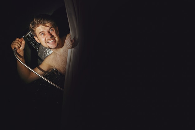 Bearded man looks funny pouring shower over himself in black bathroom