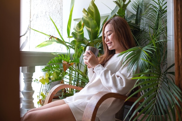 Photo a beautiful asian woman drinking hot coffee and relaxing on balcony with houseplants garden at home