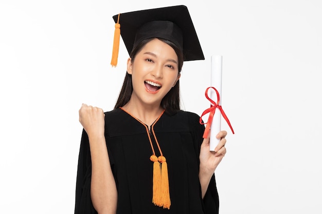 Photo beautiful attractive asian woman graduated in cap and gown smile with certificated in her hand feeling so proud and happinessisolated on white backgroundeducation success concept