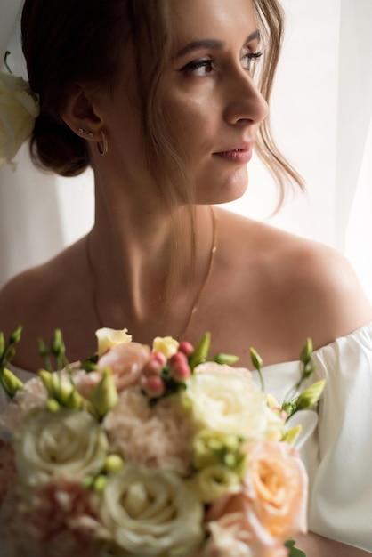 Beautiful bride with wedding bouquet near window