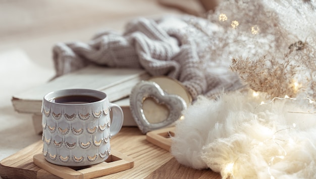 Photo a beautiful cup with a hot drink on the background of cozy things. home comfort and warmth concept.