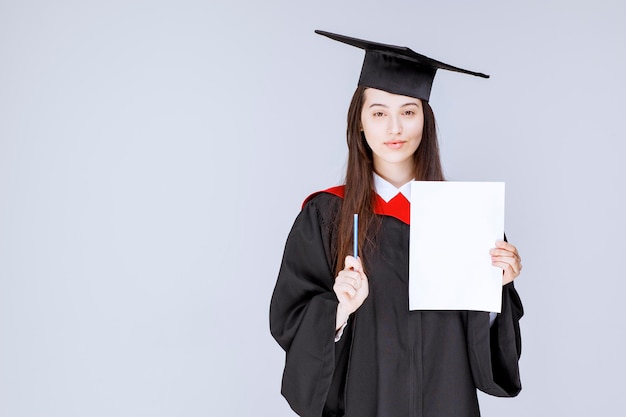 Beautiful female student showing empty paper and holding pen. High quality photo