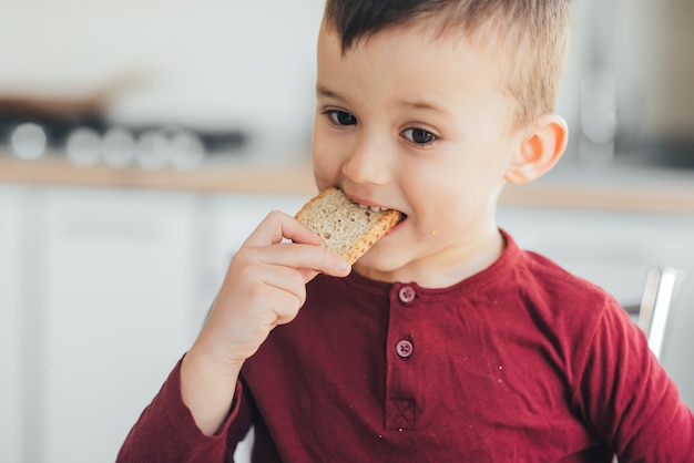 Beautiful little boy in the kitchen eating a piece of bread hungry