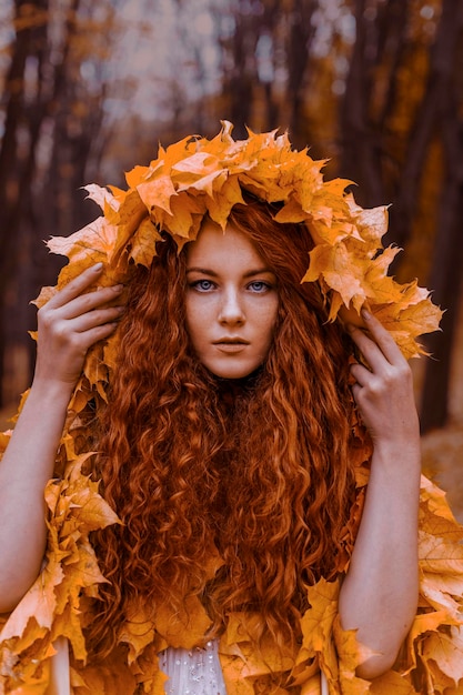 Beautiful redhead girl as a autumn in leaf cloak in forest