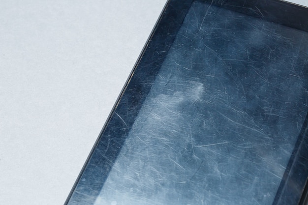 Black scratched tablet with a protective film on a gray background. Protect your device screen