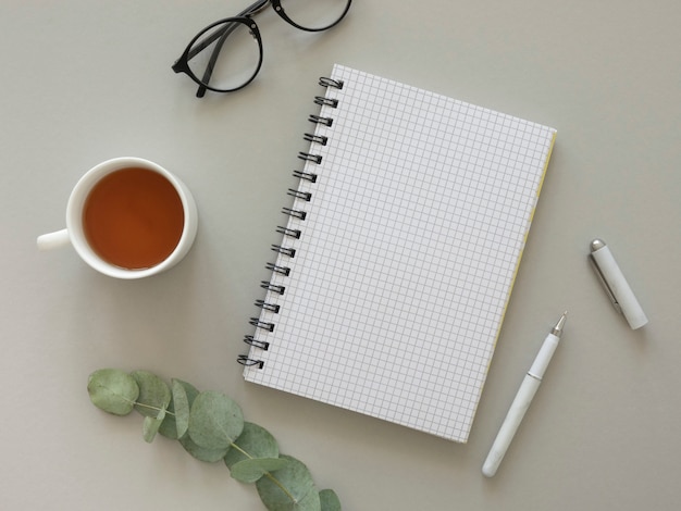 Photo blogger workplace flat lay mockup. hipster's glasses and opened notebook with empty paper sheet, tea and eucalyptus.