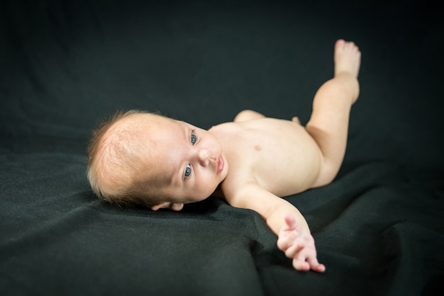 Blue eyed naked baby lying on black fabric