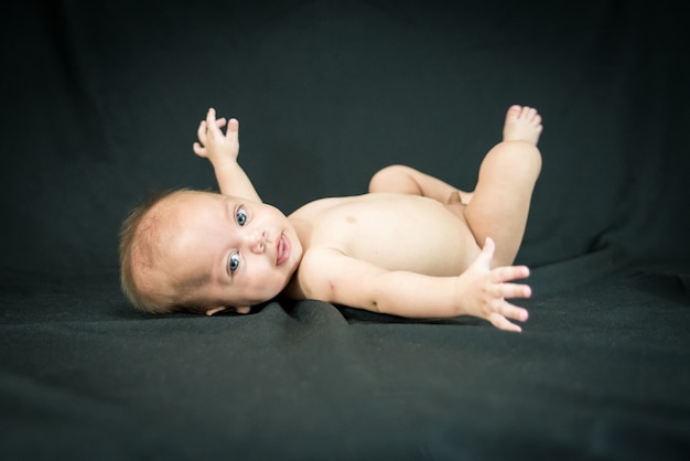 Blue eyed naked baby lying on black fabric