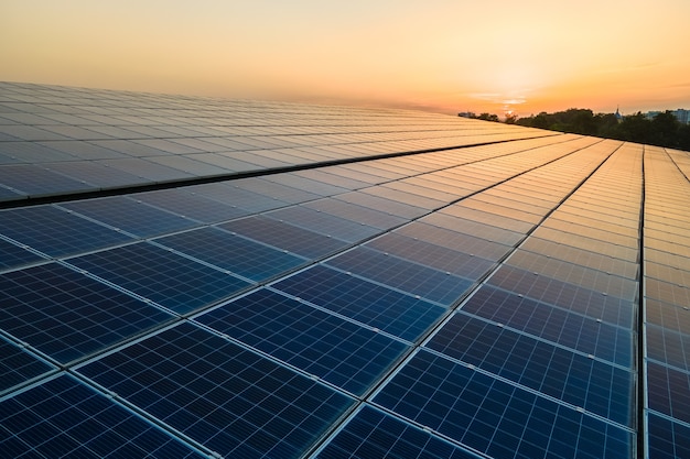 Blue photovoltaic solar panels mounted on building roof for producing clean ecological electricity at sunset. Production of renewable energy concept.