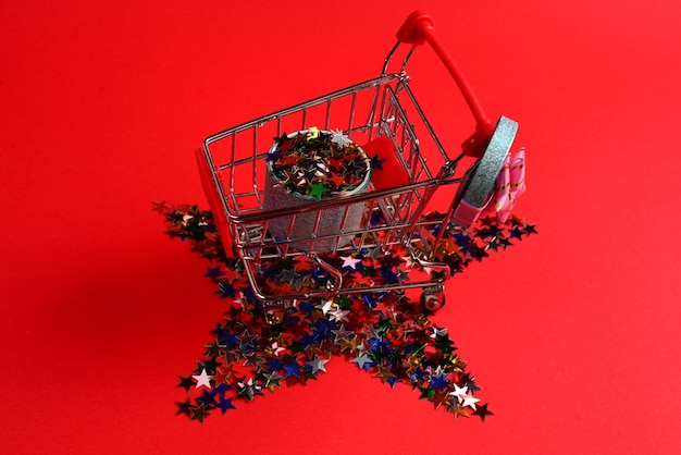 Blue present box with pink bow in a shopping cart and confetti on a red background