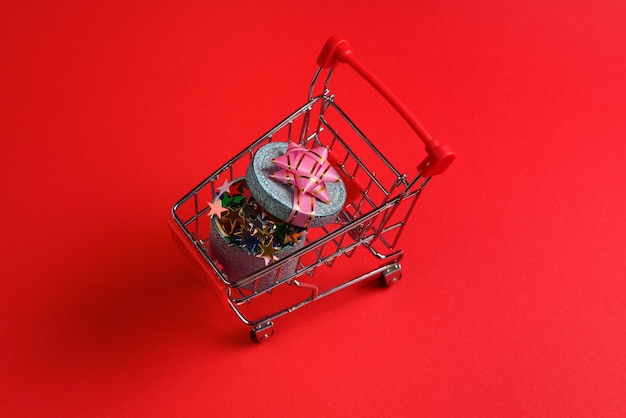 Blue present box with pink bow in a shopping cart on a red background