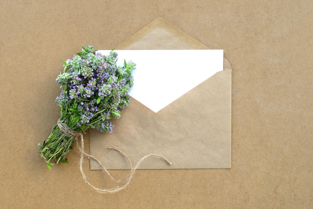 Bouquet of wildflowers and envelope with blank card on a cardboard background bunch of thyme flowers