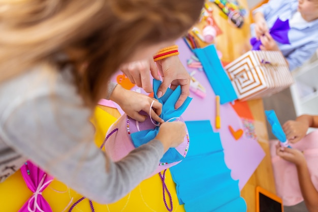 Box with bows. Dark-haired girl and helpful teacher decorating present box with paper bows