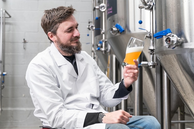 Brewer wearing white coat controlling process of beer fermentation while working at modern beer factory