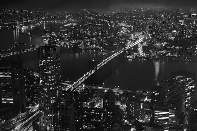 Buildings, skyscrapers, streets, the Brooklyn and Manhattan bridges at night in New York City. Aerial view. Black and white