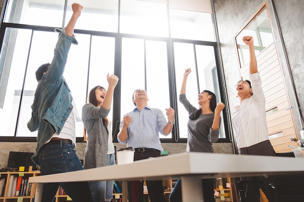 Photo business people excited happy smile throw papers documents fly in air businesspeople sitting at office desk hold hands arms up success team concept after sign contract