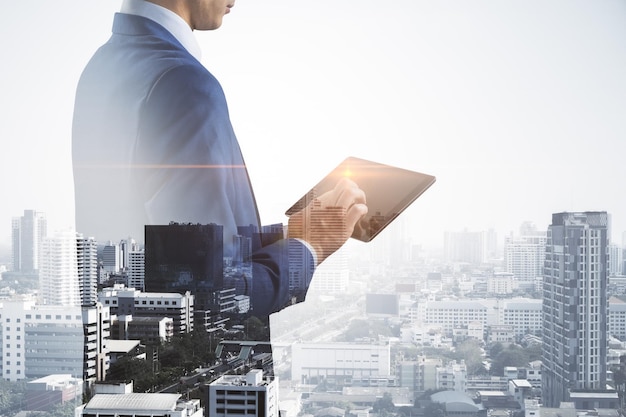 Business technology concept with businessman using modern digital tablet on city skyline background double exposure