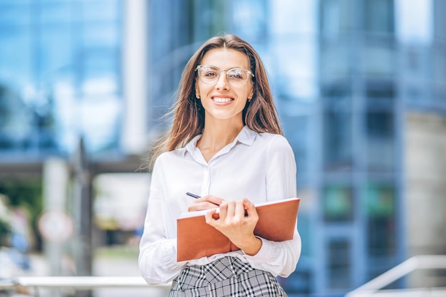 Business woman outdoors near modern business center with notebook.