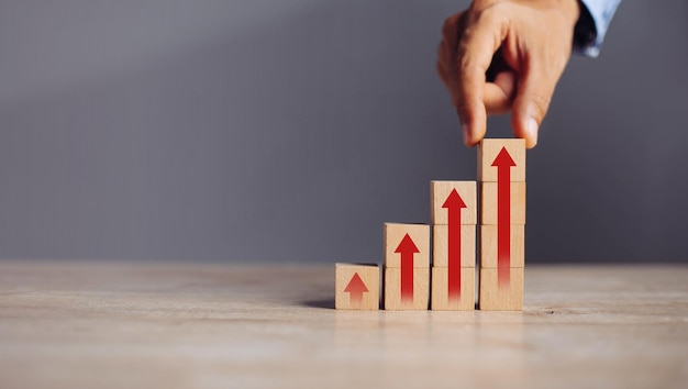 Businessman hand arranging wood block stacking as step stair with arrow upconcept for business growth success process