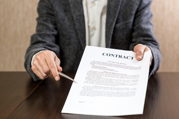 Businessman handing over a contract for signature offering a ballpoint pen in his hand