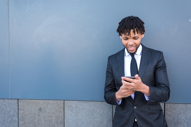 Businessman using smartphone at street blue wall