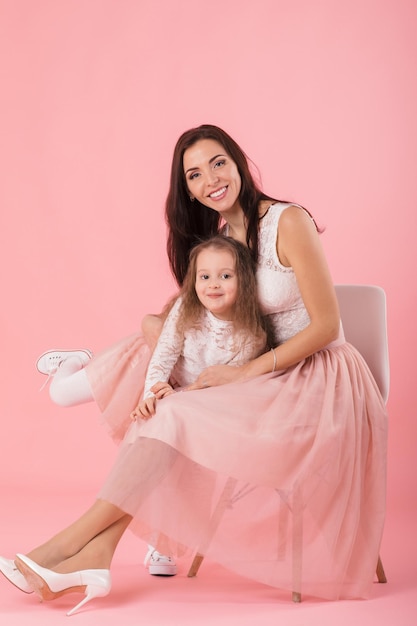 Charming mother and smiling daughter on pink background