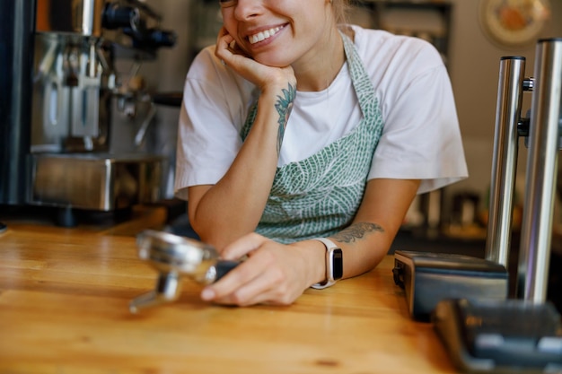 A cheerful barista is happily smiling at the coffee shop counter as customers enjoy their drinks