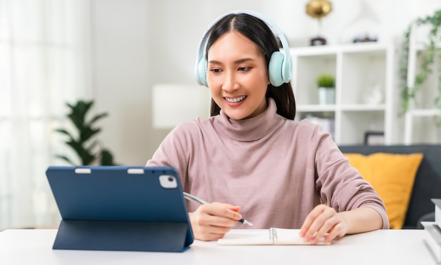 Photo cheerful beautiful asian woman wearing headphones and look to digital tablet at video calling meeting and study online on the internet.