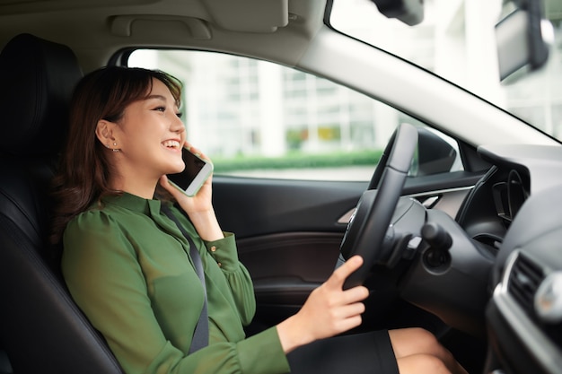 Photo 車を運転してスマートフォンで話す陽気な若い女性