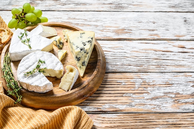 Photo cheese plate with camembert, brie and blue cheese with grapes. white wooden background. top view. copy space