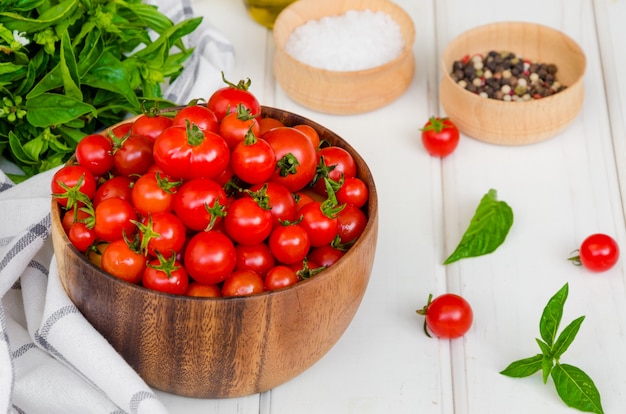 Photo cherry tomatoes, basil herb, olive oil and salt in on a wooden bowl white wooden table.