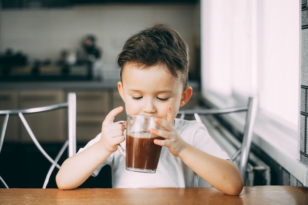 A child drinks cocoa in  kitchen or hot chocolate sweet, daylight