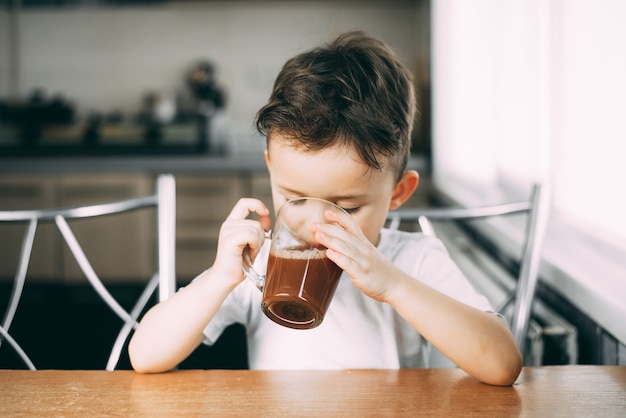 A child drinks cocoa in  kitchen or hot chocolate sweet, daylight