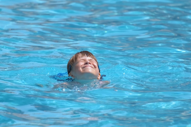 Child girl learns to swim Funny face with closed eyes on bright blue rippled water surface