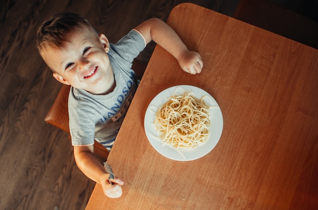 The child in the kitchen at the table eating macaroni and interesting view from the top